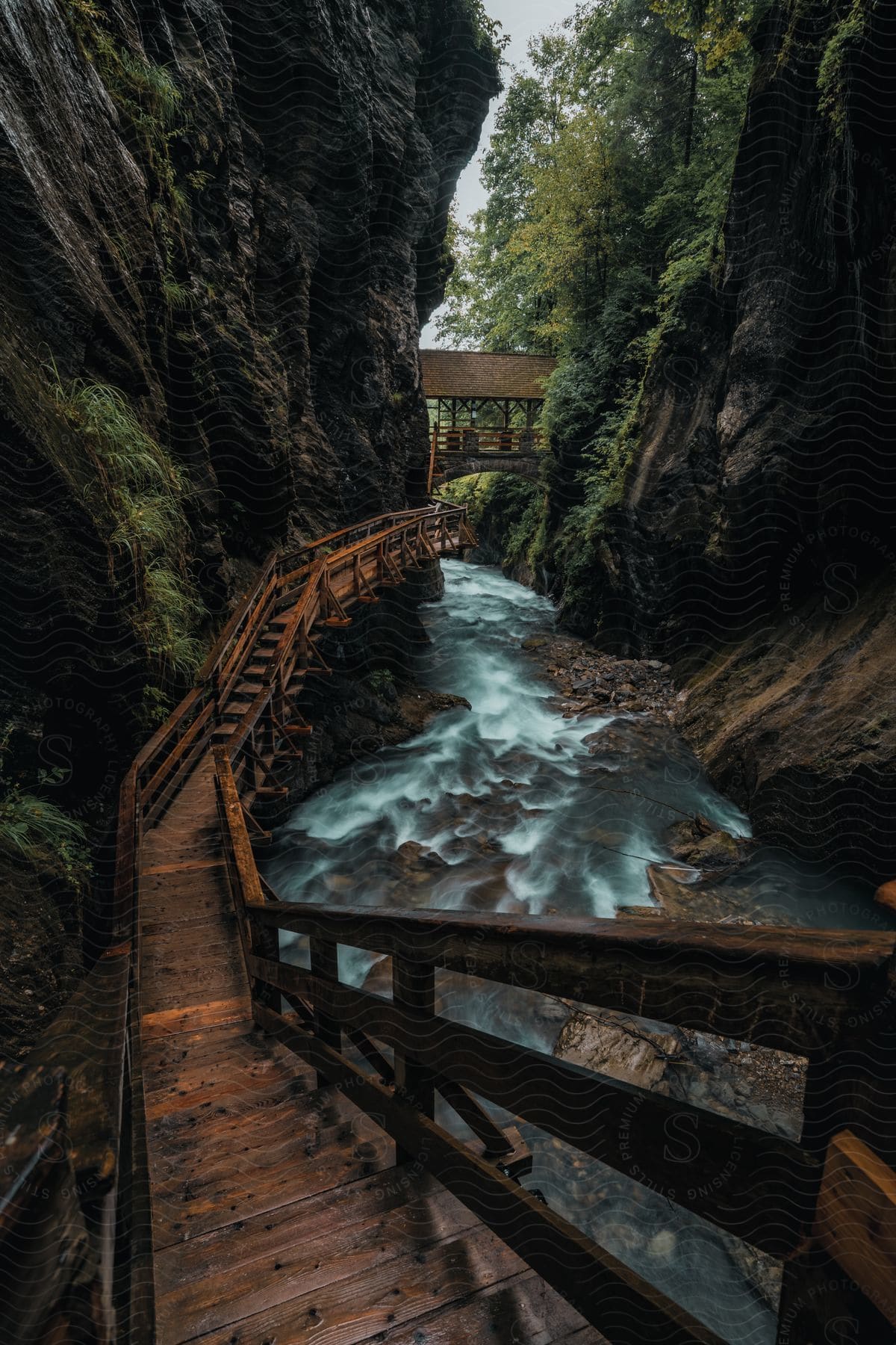 Stock photo of a wooden pathway follows a rocky wall next to a river