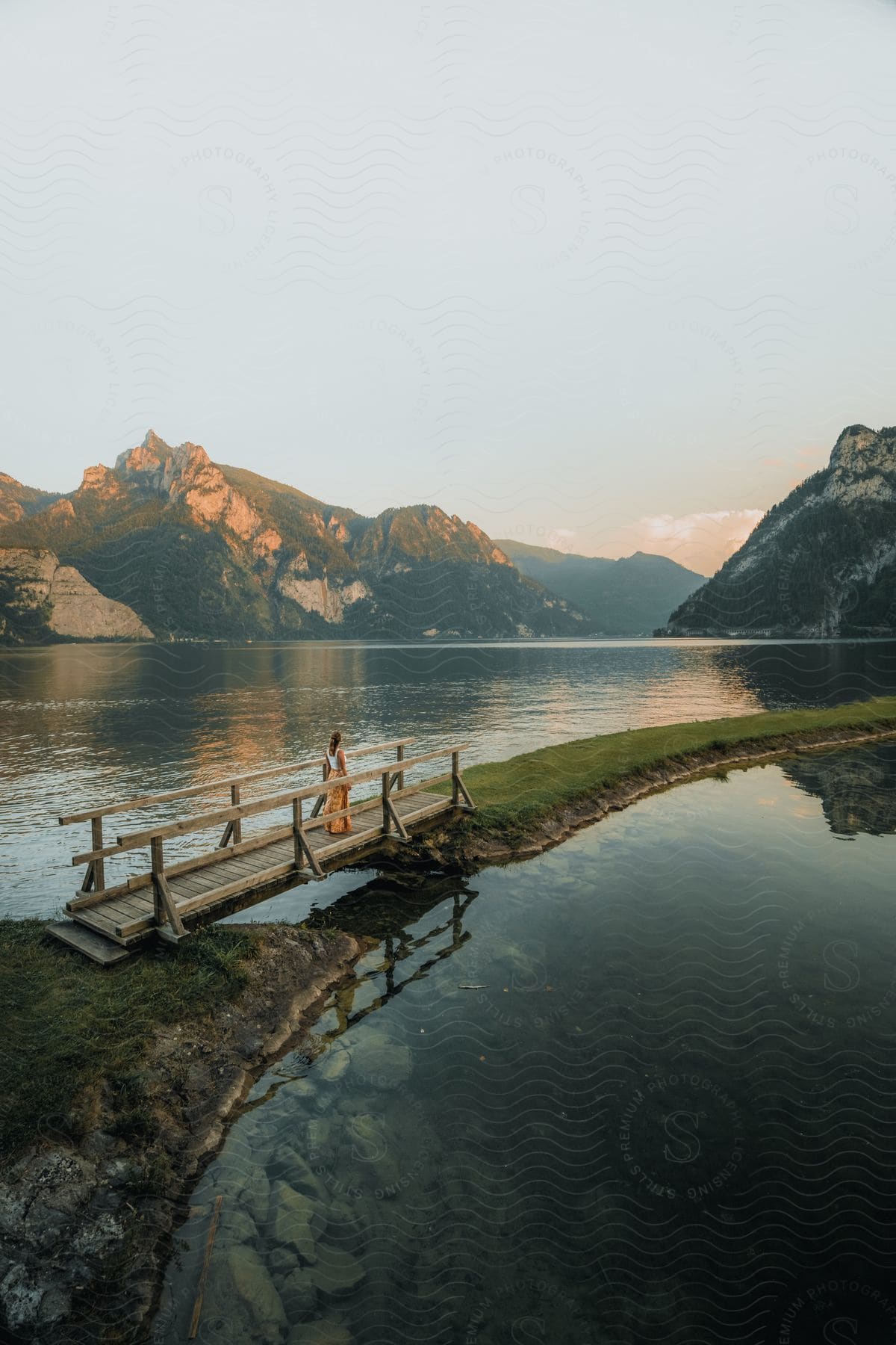 A woman walks over a bridge crossing a lake in the mountains at evening