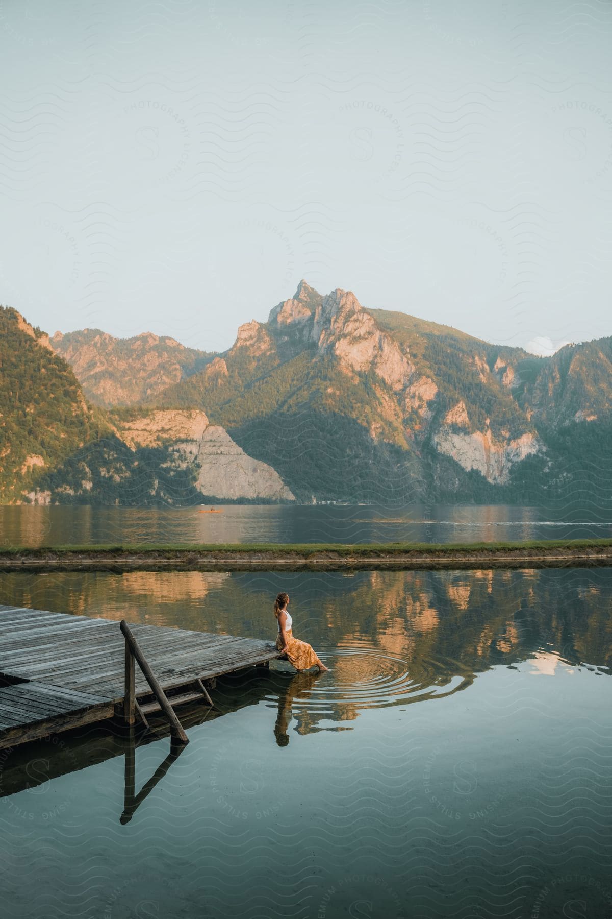 A person sitting on a dock with feet in the water of a lake