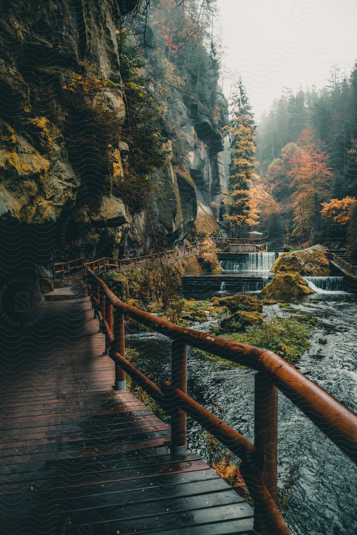 A wooden pathway leads to a waterfall next to a craggy mountainside