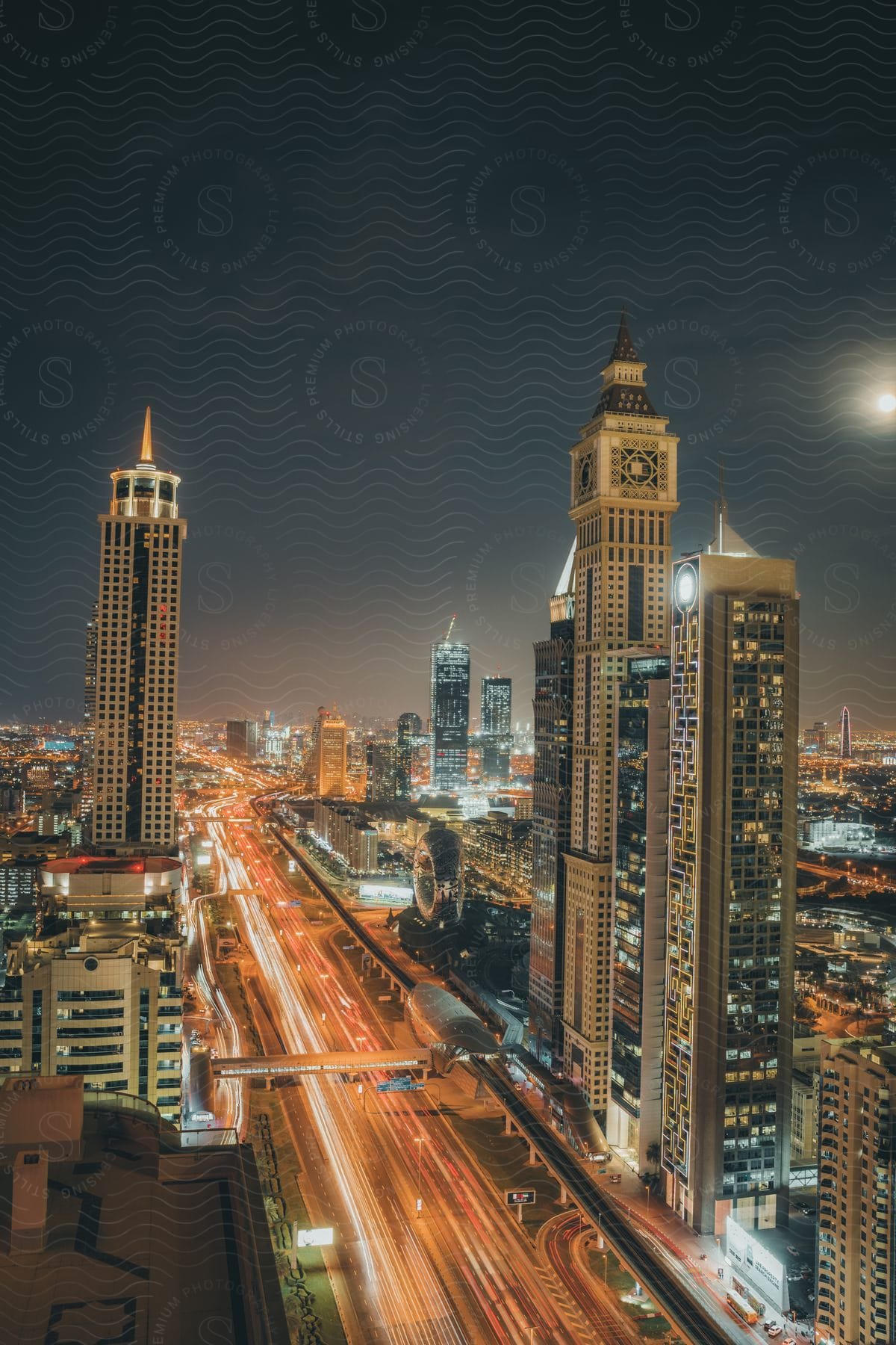 Cars and vehicles zoom up a busy highway located next to litup skyscrapers in the night sky