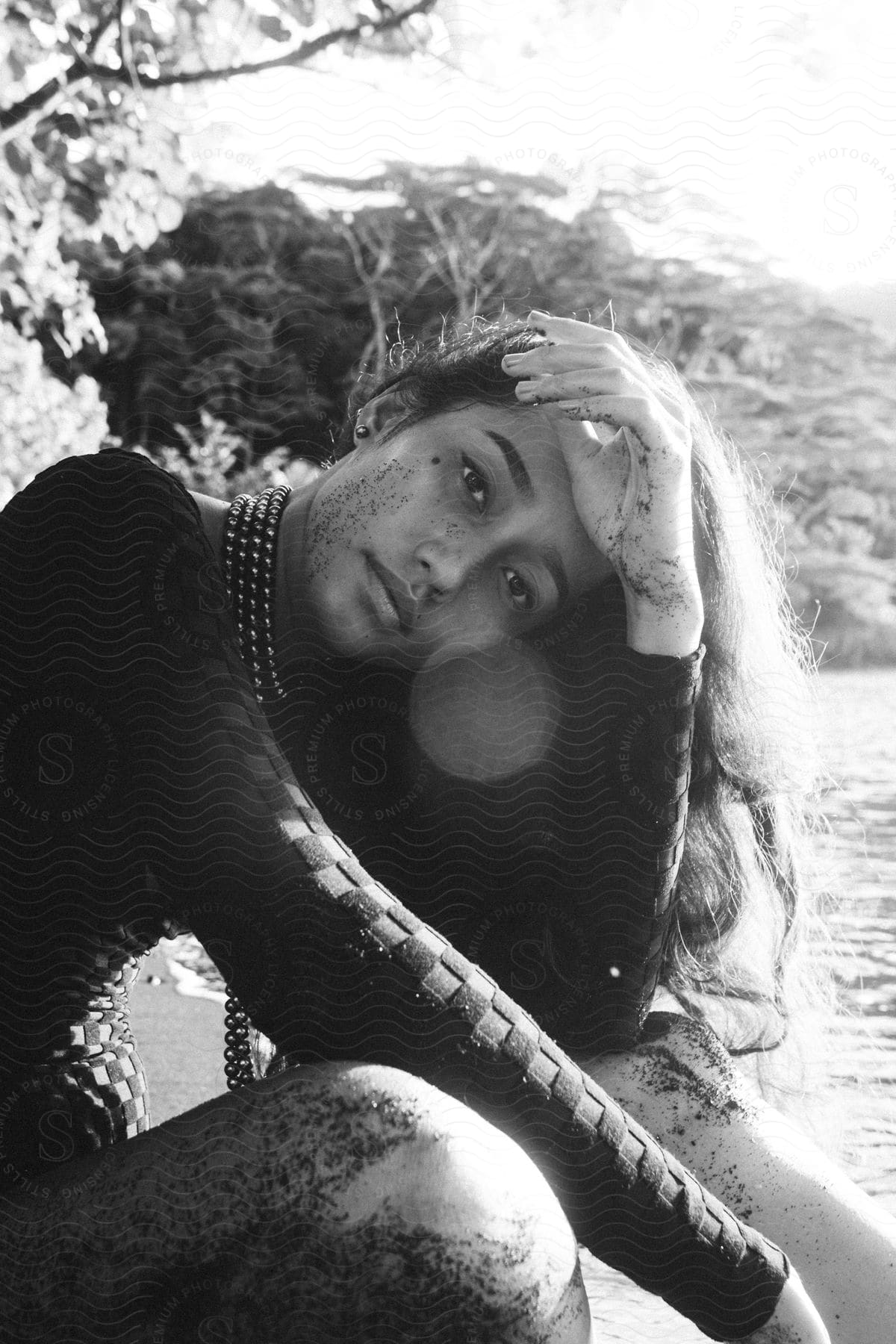 A teenage girl sits outside and poses with her hand by her forehead