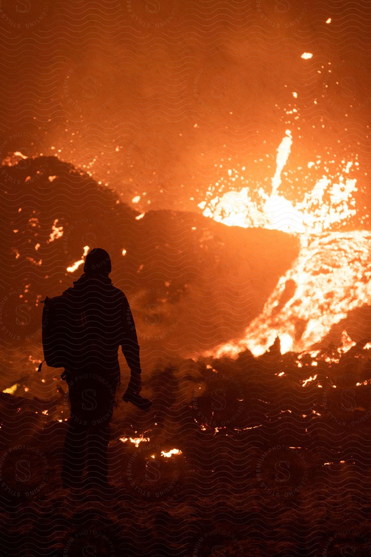 A person stands in front of erupting lava against an orange background