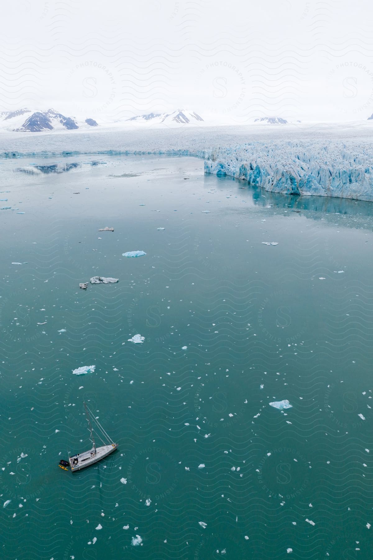 An aerial view of a boat in open waters with an ice cap on the horizon