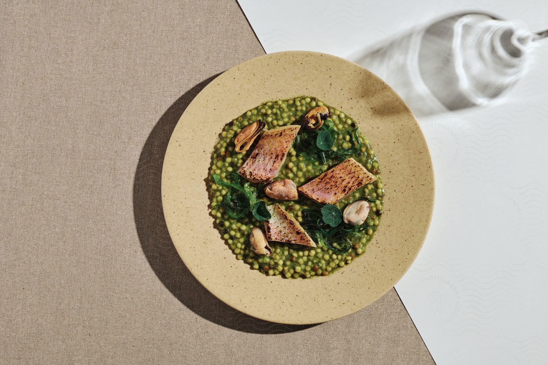 Close up of a dish called roast cod green pesto fregola on a wooden plate