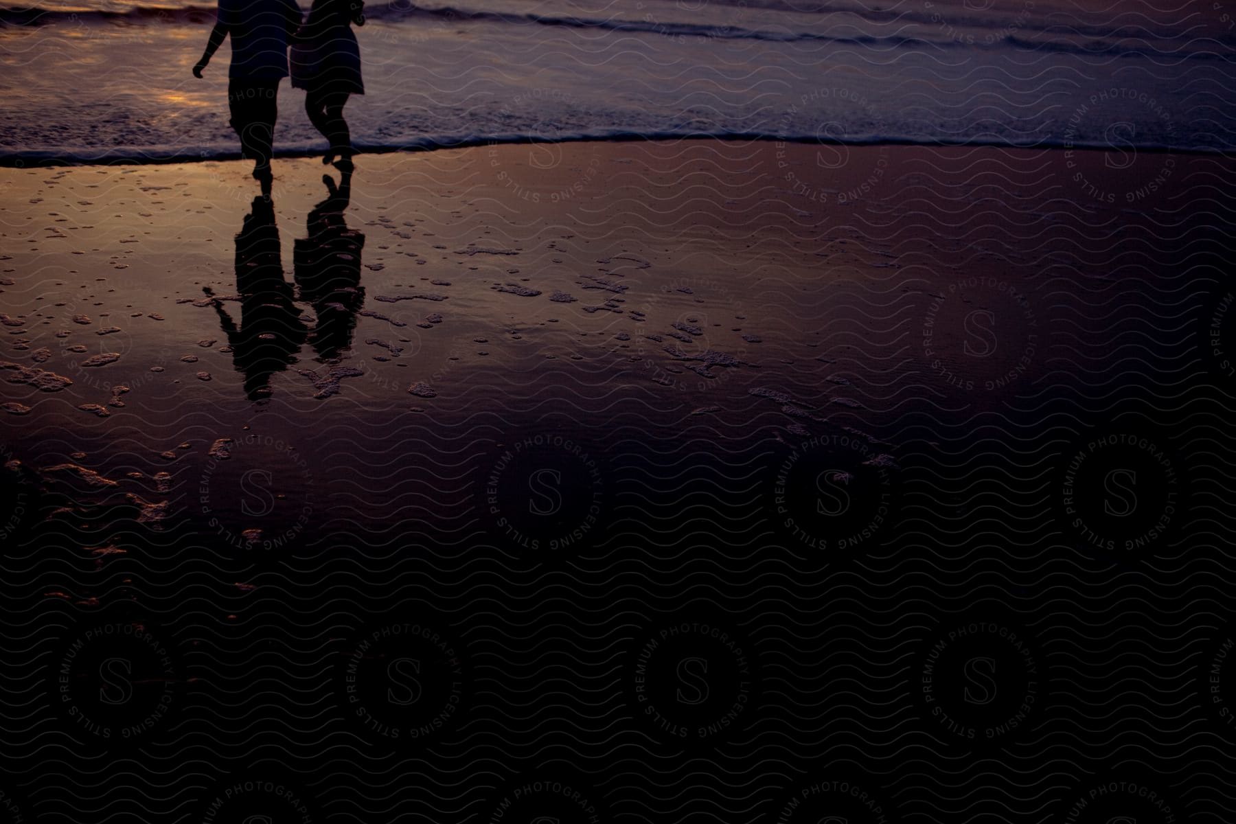 Two people jog on the beach at dusk with the tide coming in on the sand