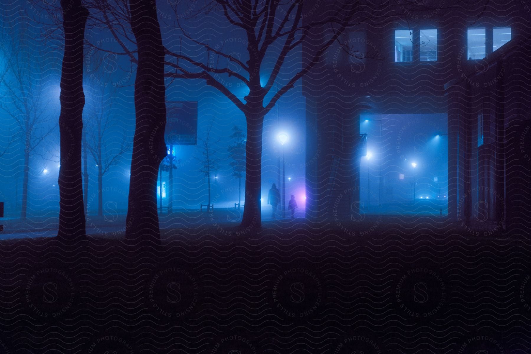 People are walking through a park on a foggy night as lights glow in the darkness