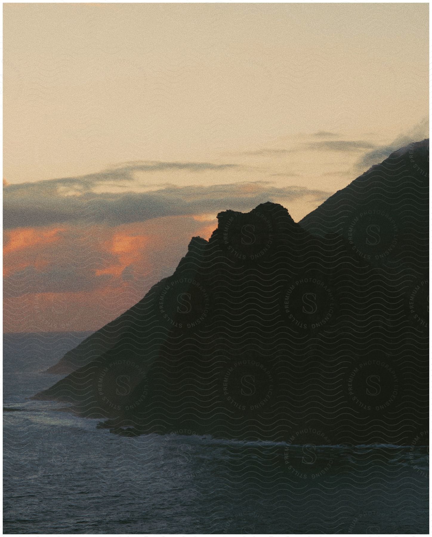 Waves splash against mountains along the coast at sunset