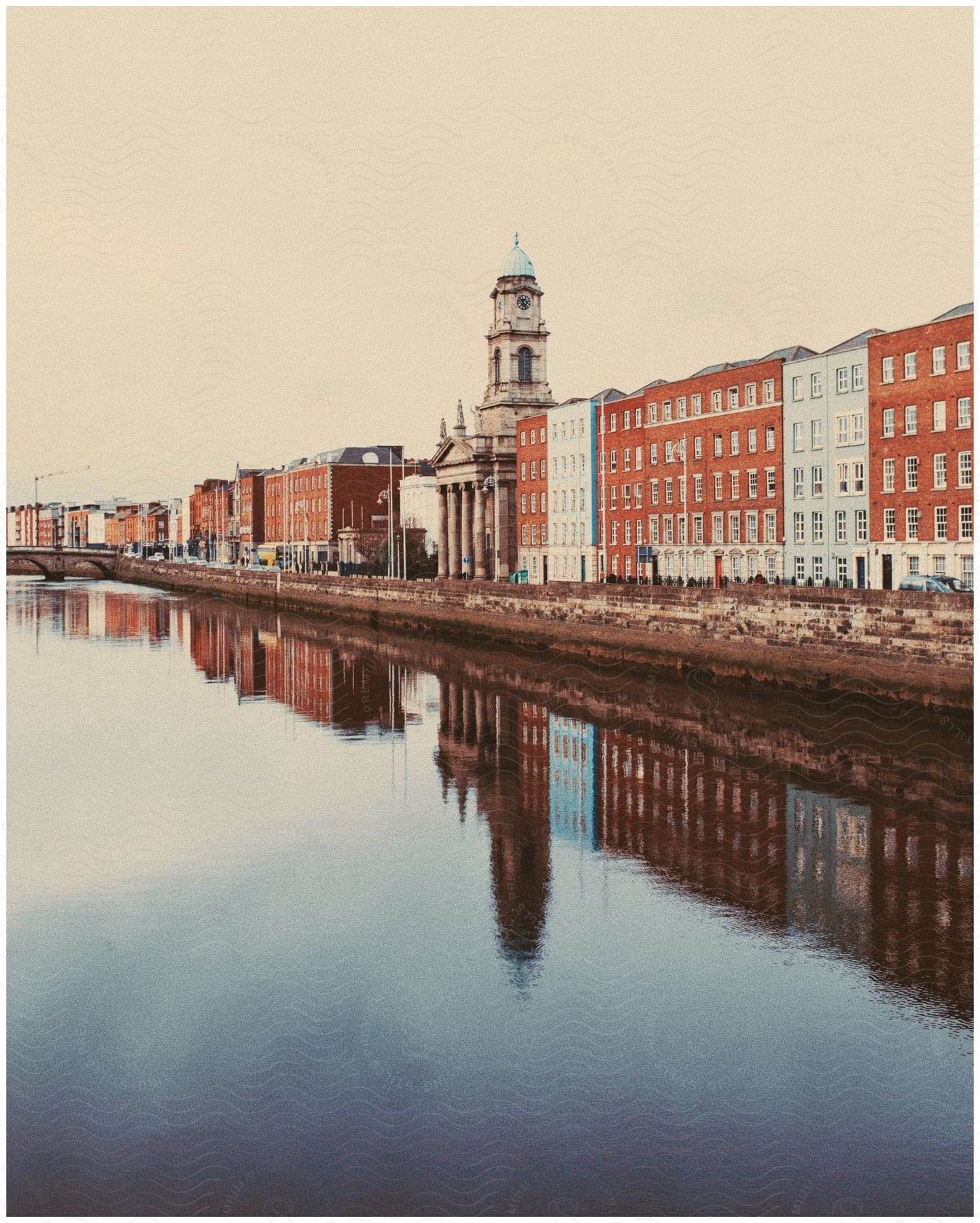 Long row of buildings next to a calm river under a cloudy sky