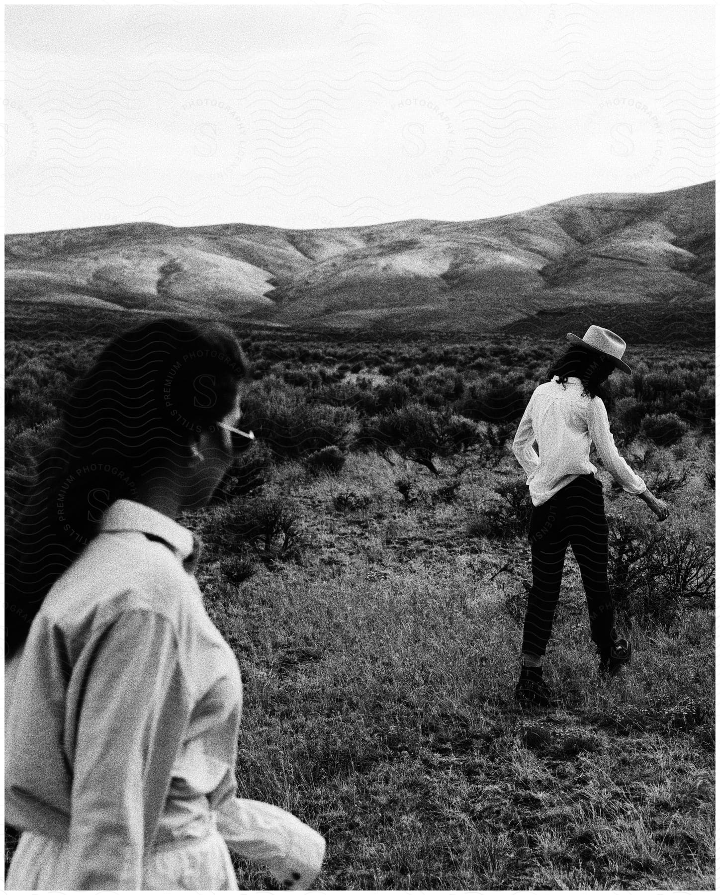 Two women walking in a grassy field with a mountain in the background captured in black and white