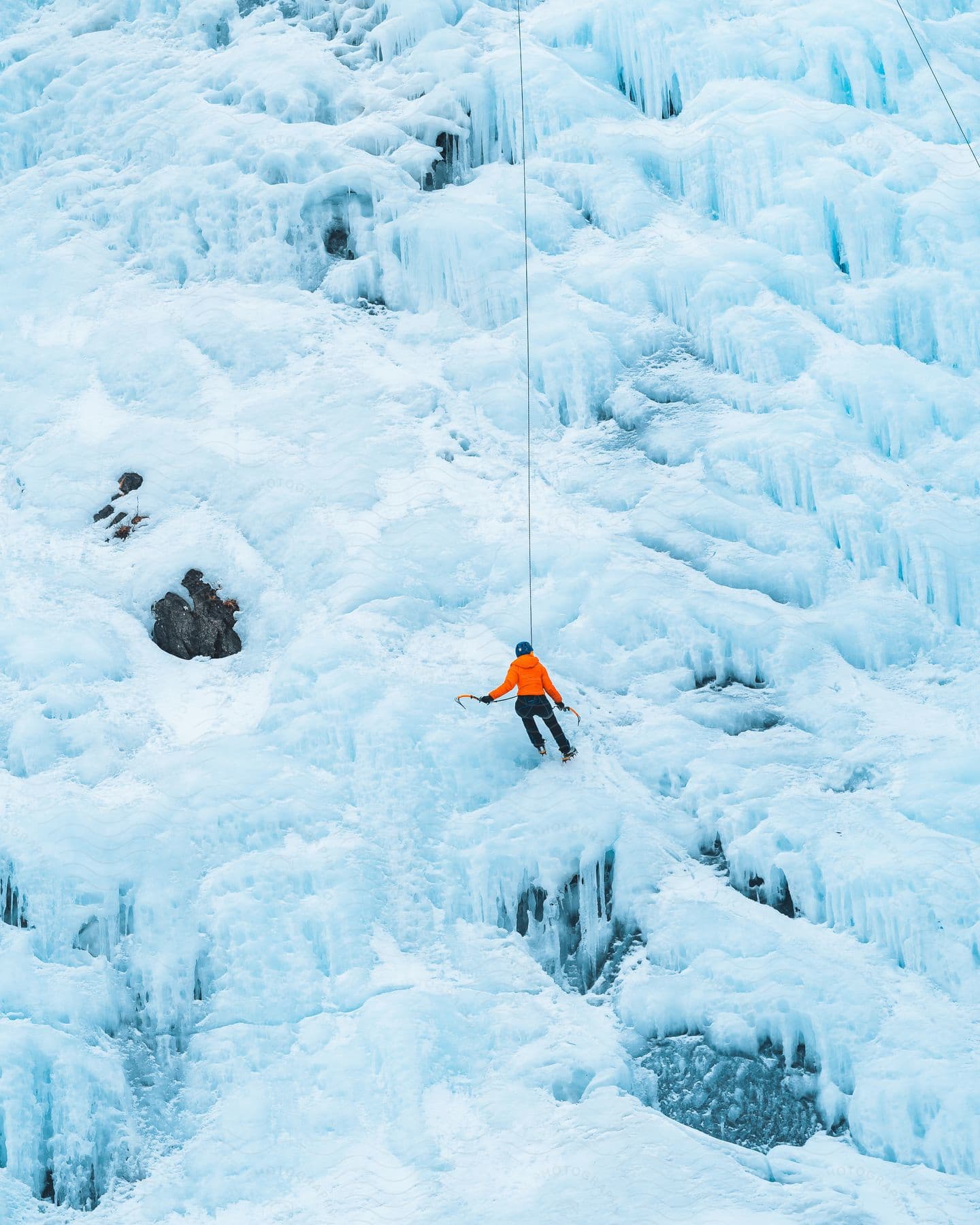 A professional mountaineer with a helmet and orange coat is attached to a rope while climbing a mountain