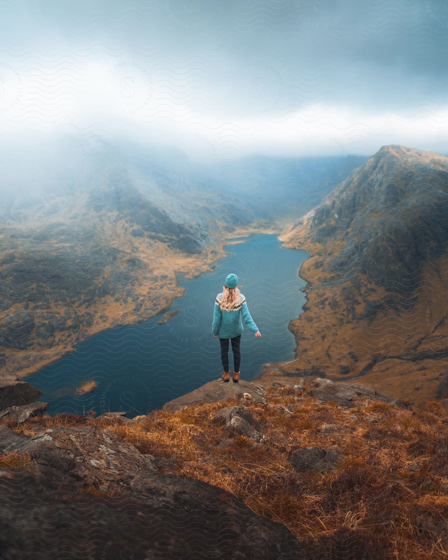 A person stands near a cliff overlooking a lake in the mountain wilderness