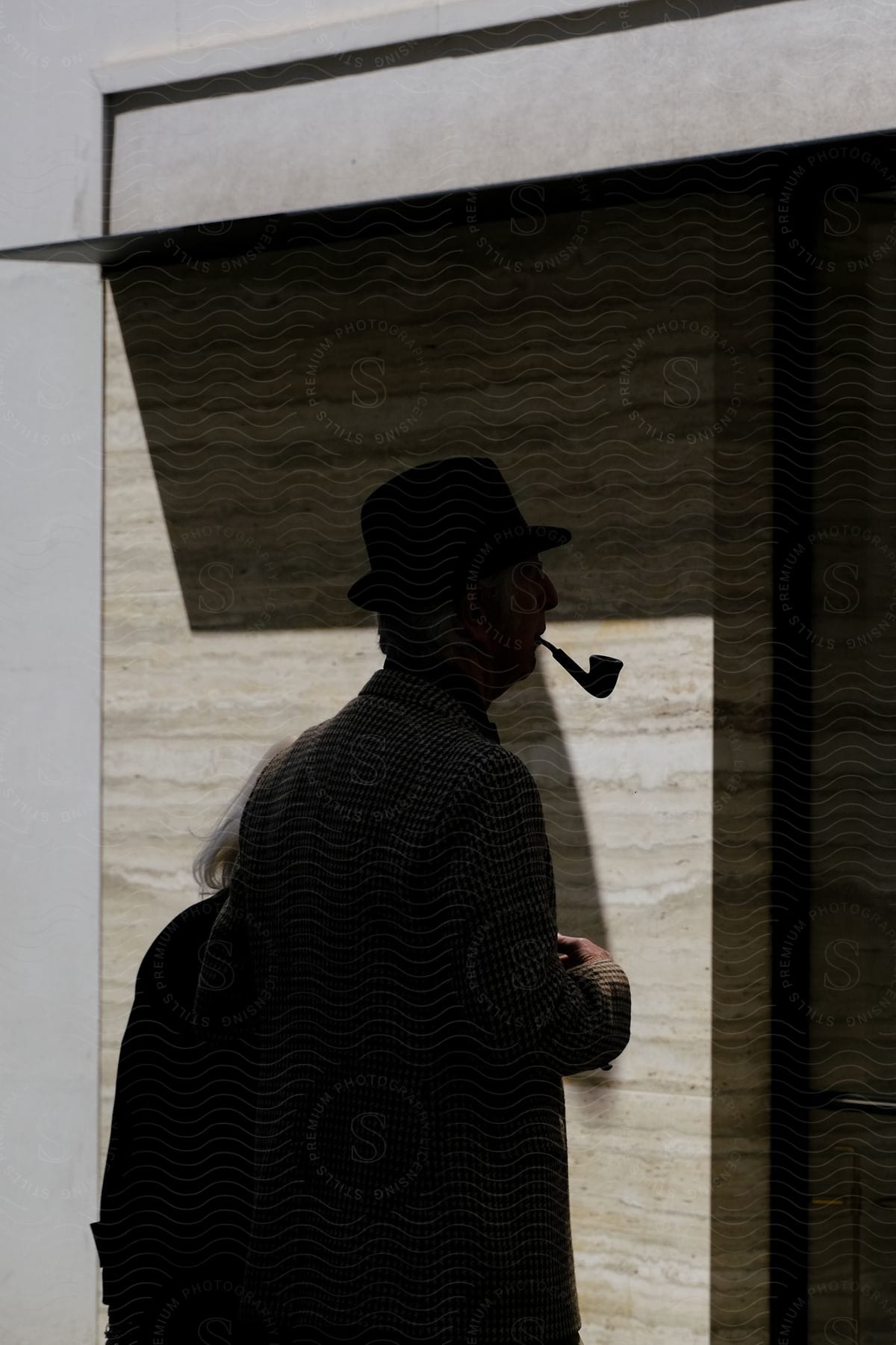 An older man and woman standing outside in front of a building the man with a pipe in his mouth