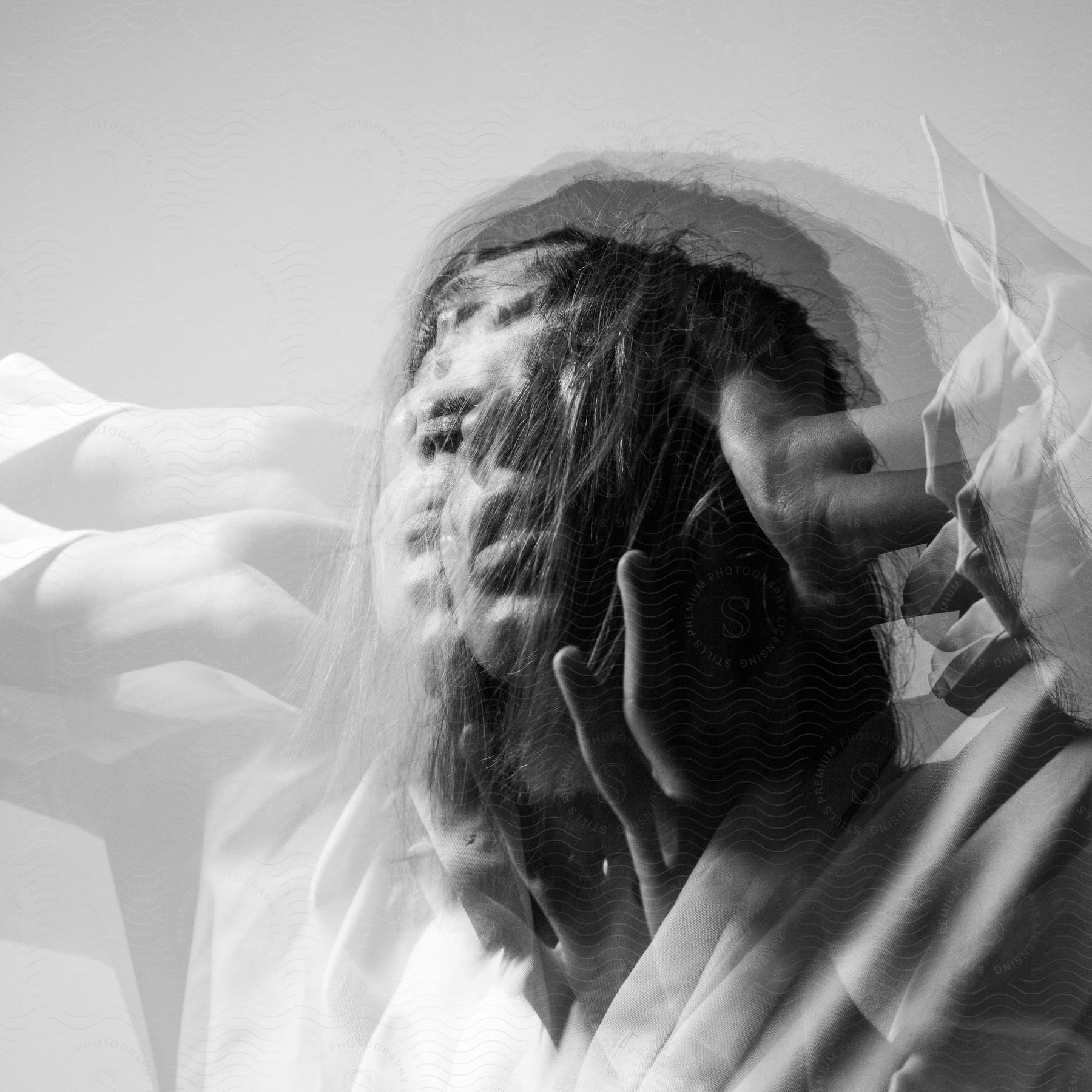 A woman with dark hair and white shirt holds her head looking up