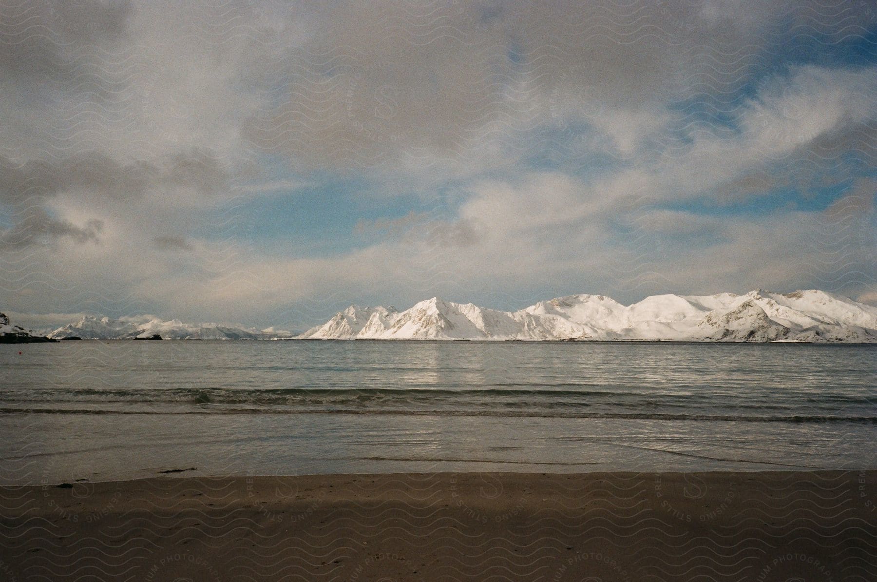 Snowy mountain range and body of water seen from beach