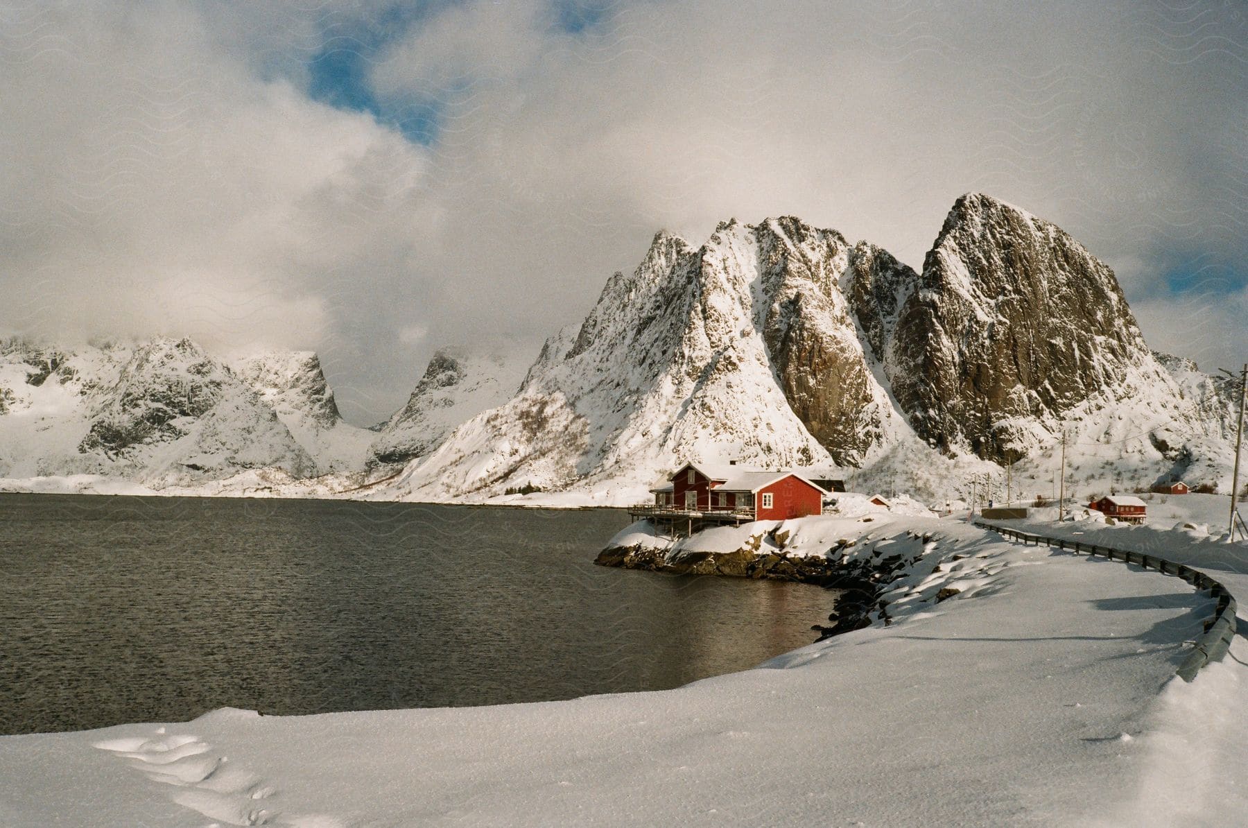 Red house overlooking coast on snowcovered rocks in winter with snowcovered mountains in the backdrop