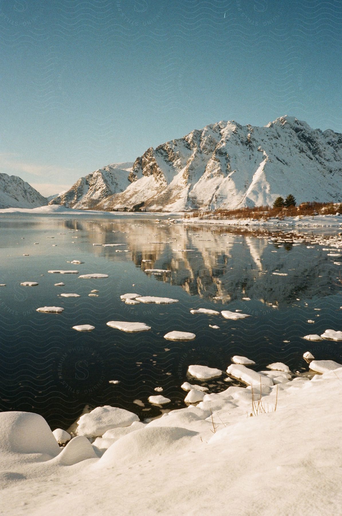 Snow and ice float on a lake surrounded by mountains on a clear day