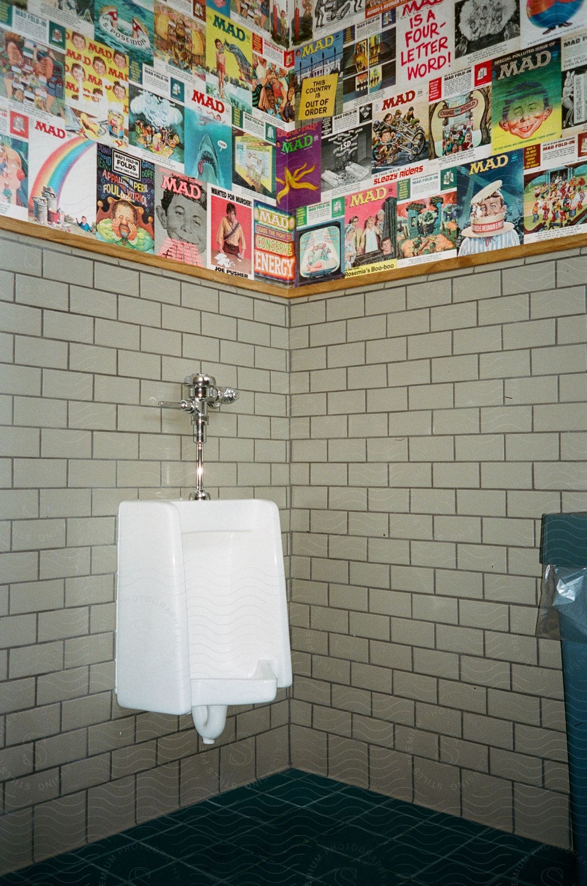 A bathroom urinal decorated with covers from mad magazine