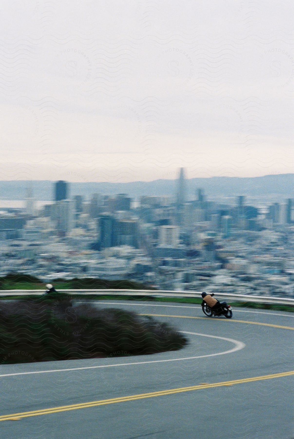 Motorcycle drives down a road in the hills next to the city at evening