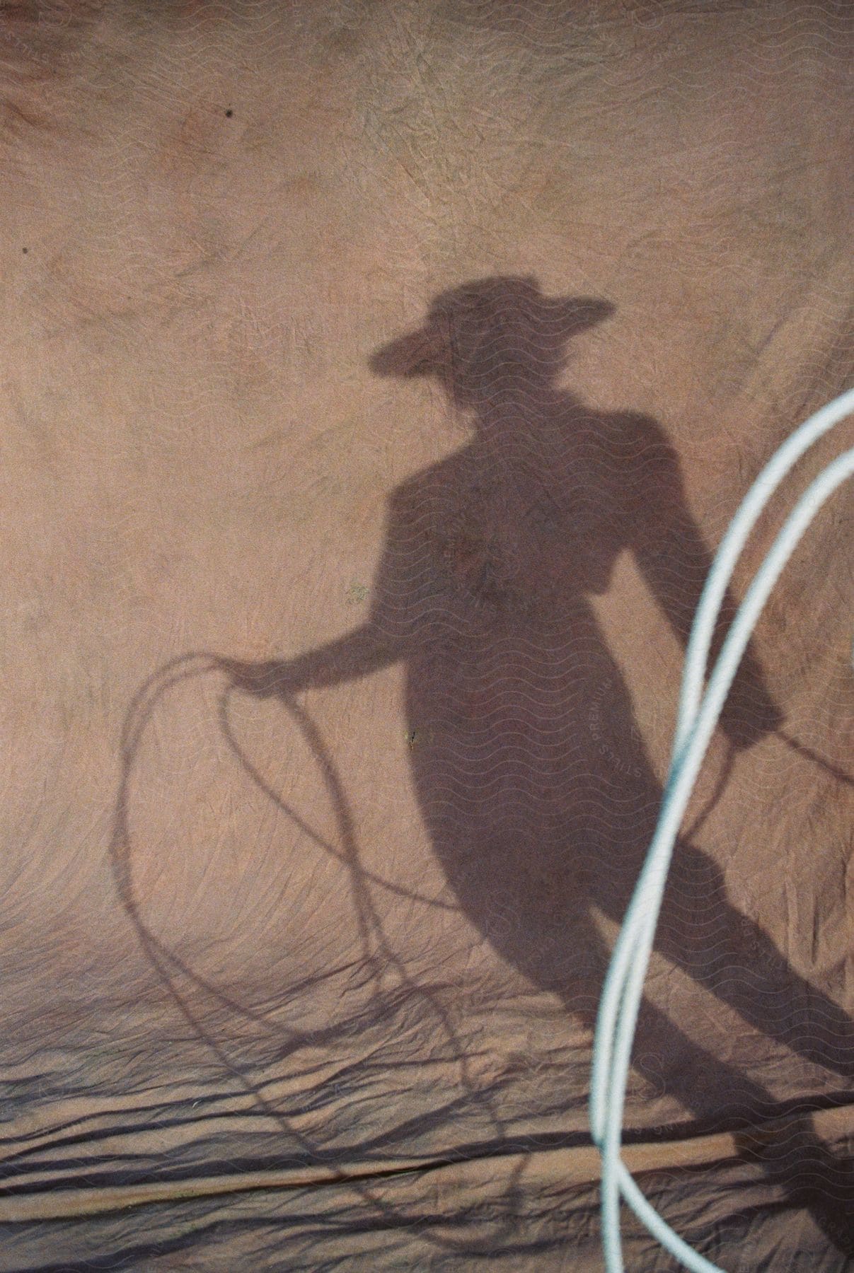 A determined woman wearing a hat jacket and pants holds a rope and casts a shadow on the ground