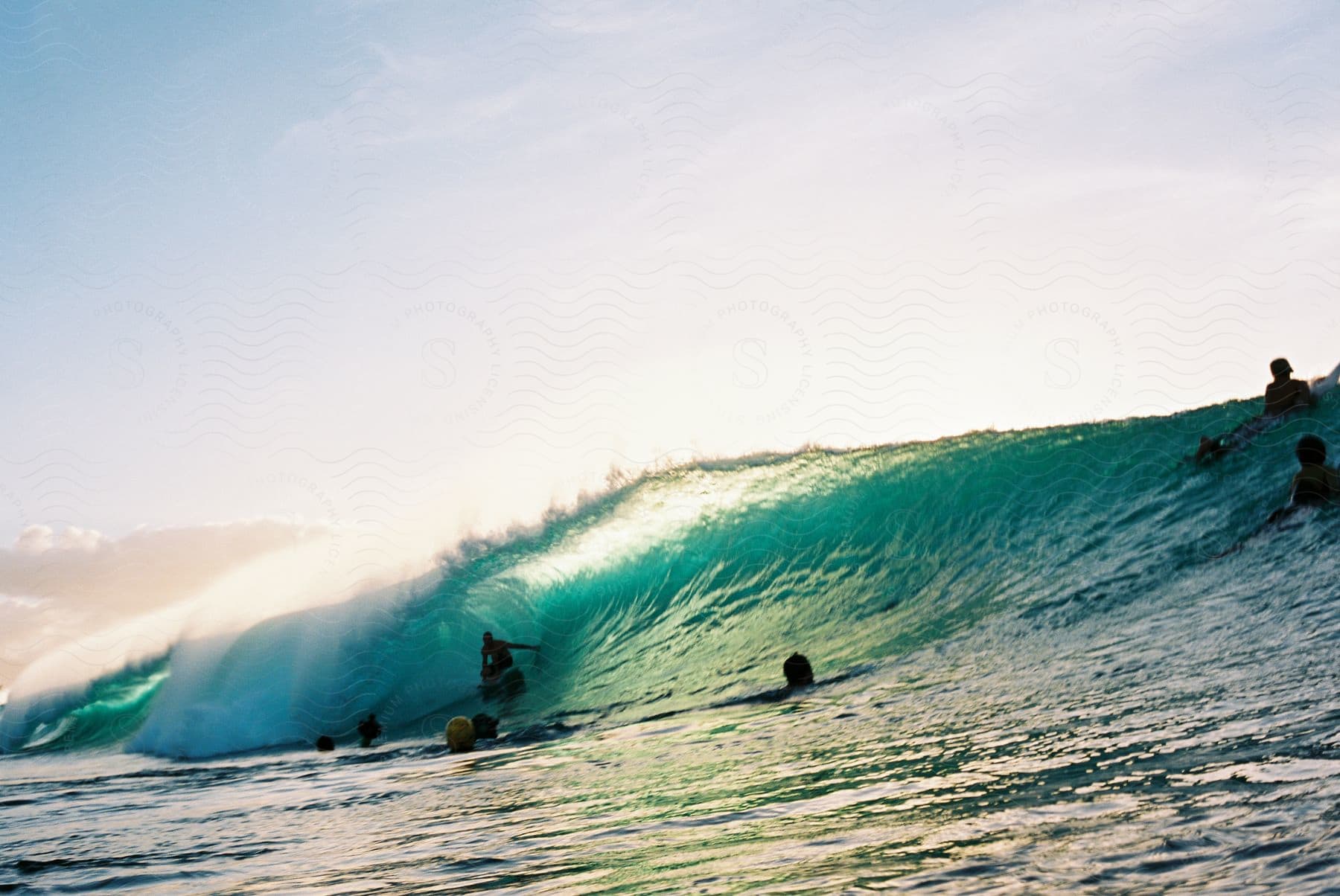 A group of surfers ride a large wave towards the coast in the evening