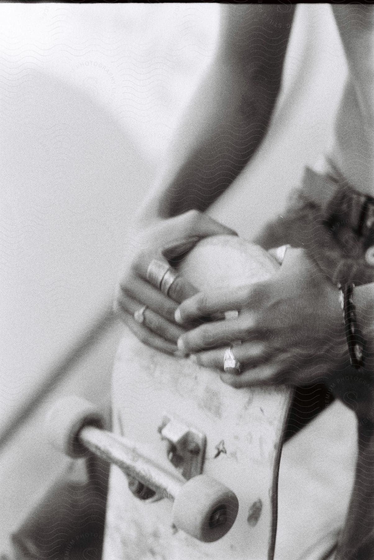 A person holding a skateboard with rings and bracelets on