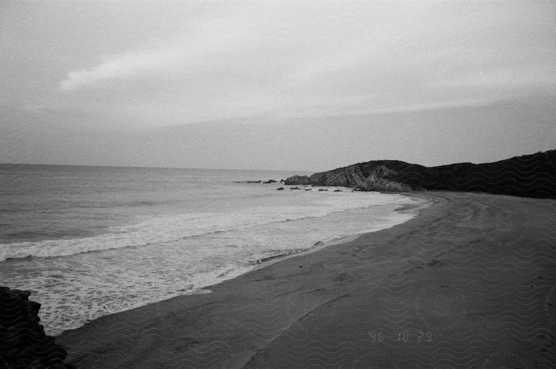 A blackandwhite depiction of a coastal promontory with a cloudy sky and water resources