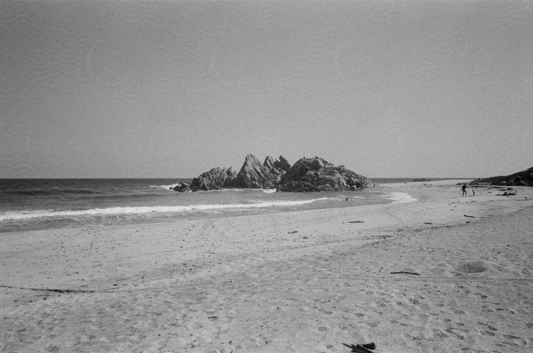 A person stands on the beach near a rocky outcropping