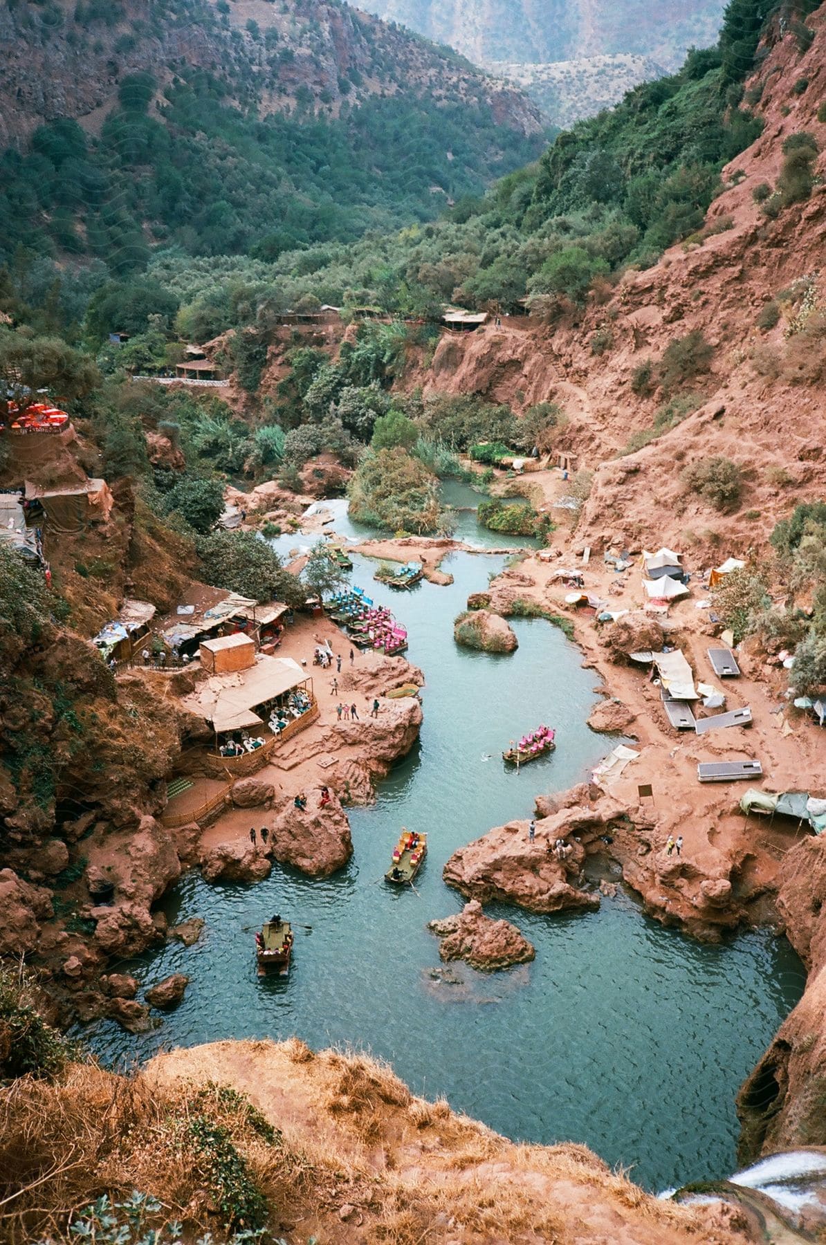 A small town surrounded by mountains and forests with a lake filled with small boats