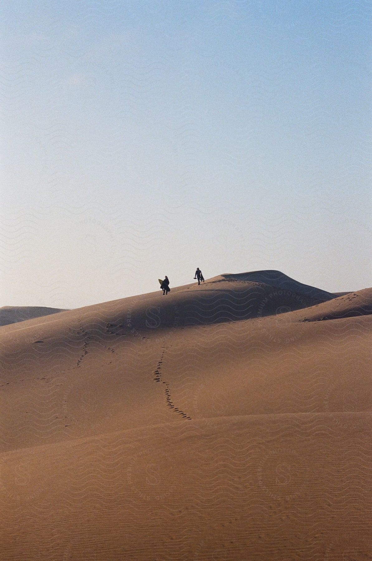 Two people walking on a sand dune on a clear day