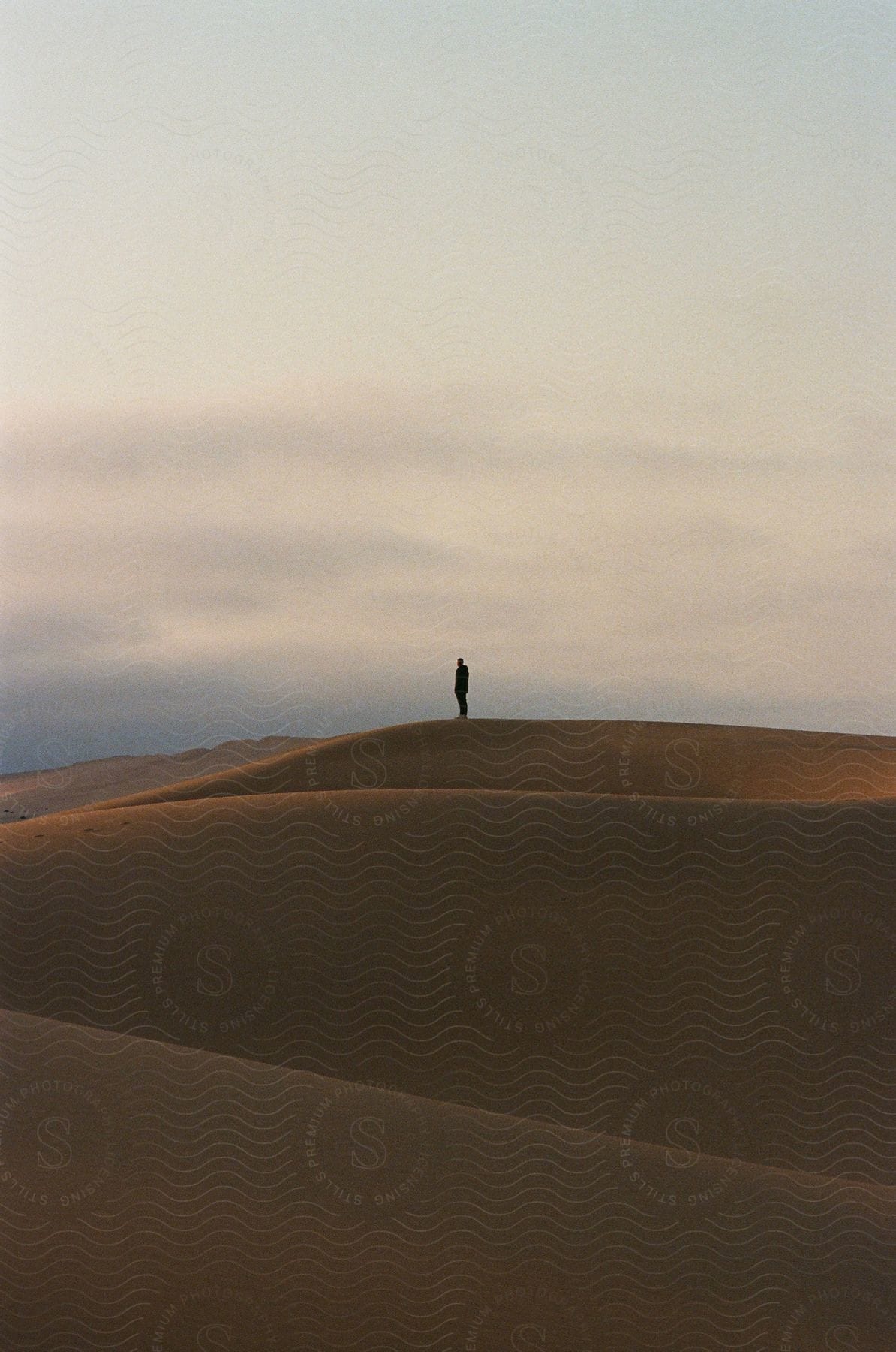 A man standing on a sand dune is silhouetted against the sky in the desert at dusk