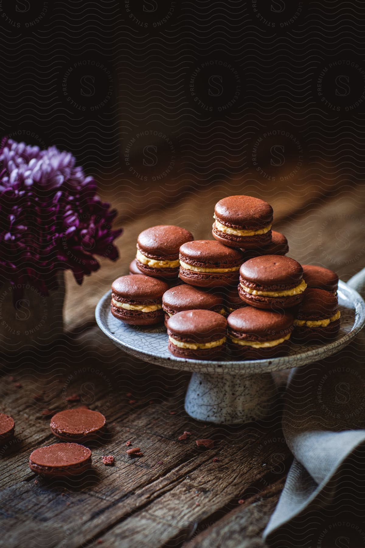 Chocolate macarons are displayed on a platter next to a purple potted plant