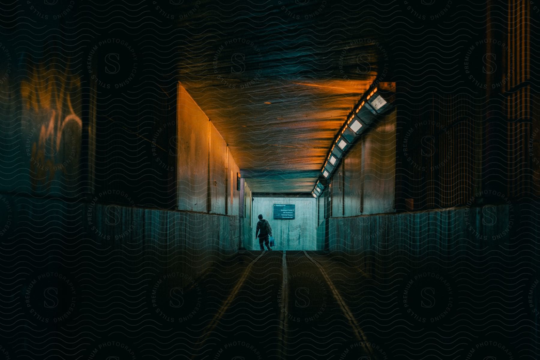 A man is turning the corner to leave at the far end of a dimly lit pedestrian tunnel