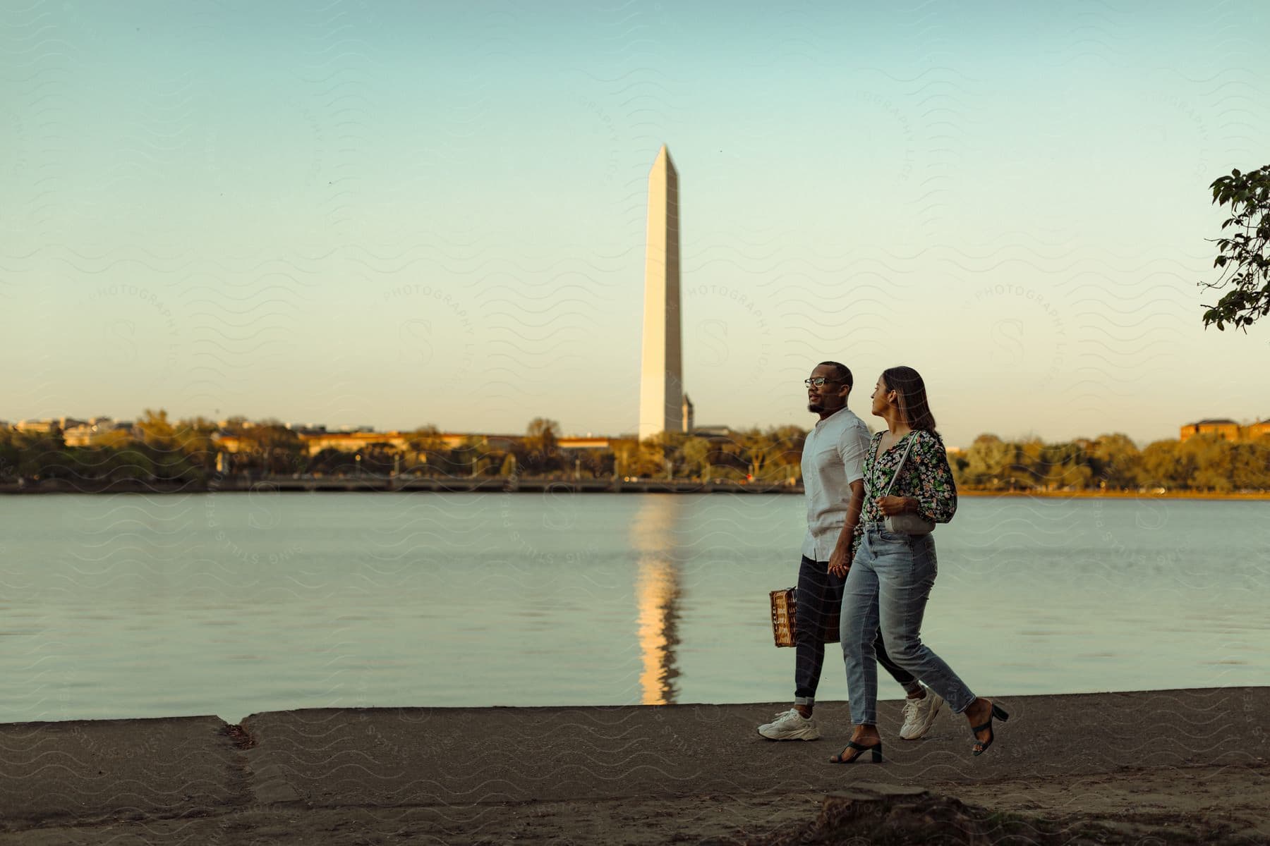 A man and woman walk near a reflecting pool with a monument in the background