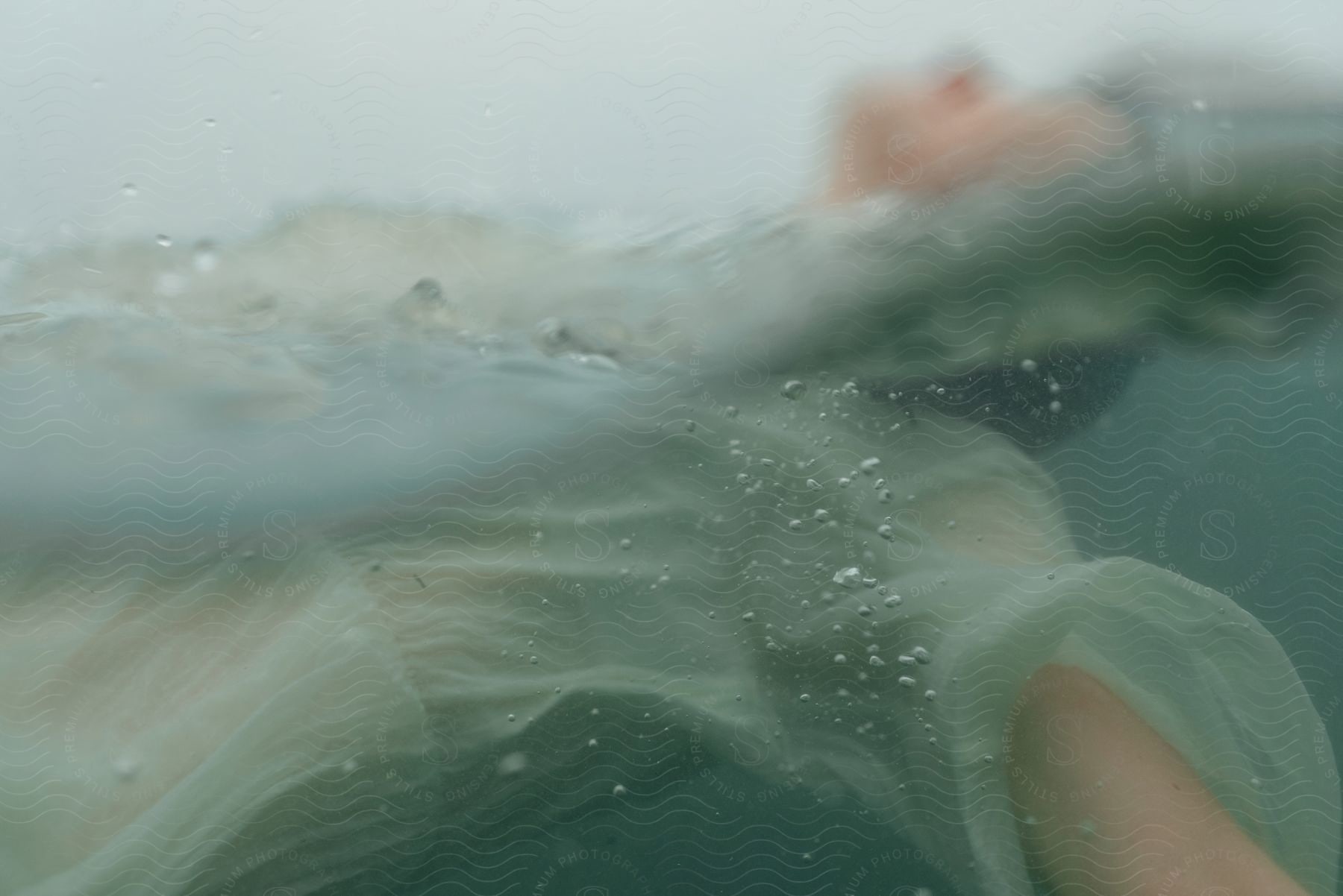 A blurry person floating in water half way wearing a sheer dress