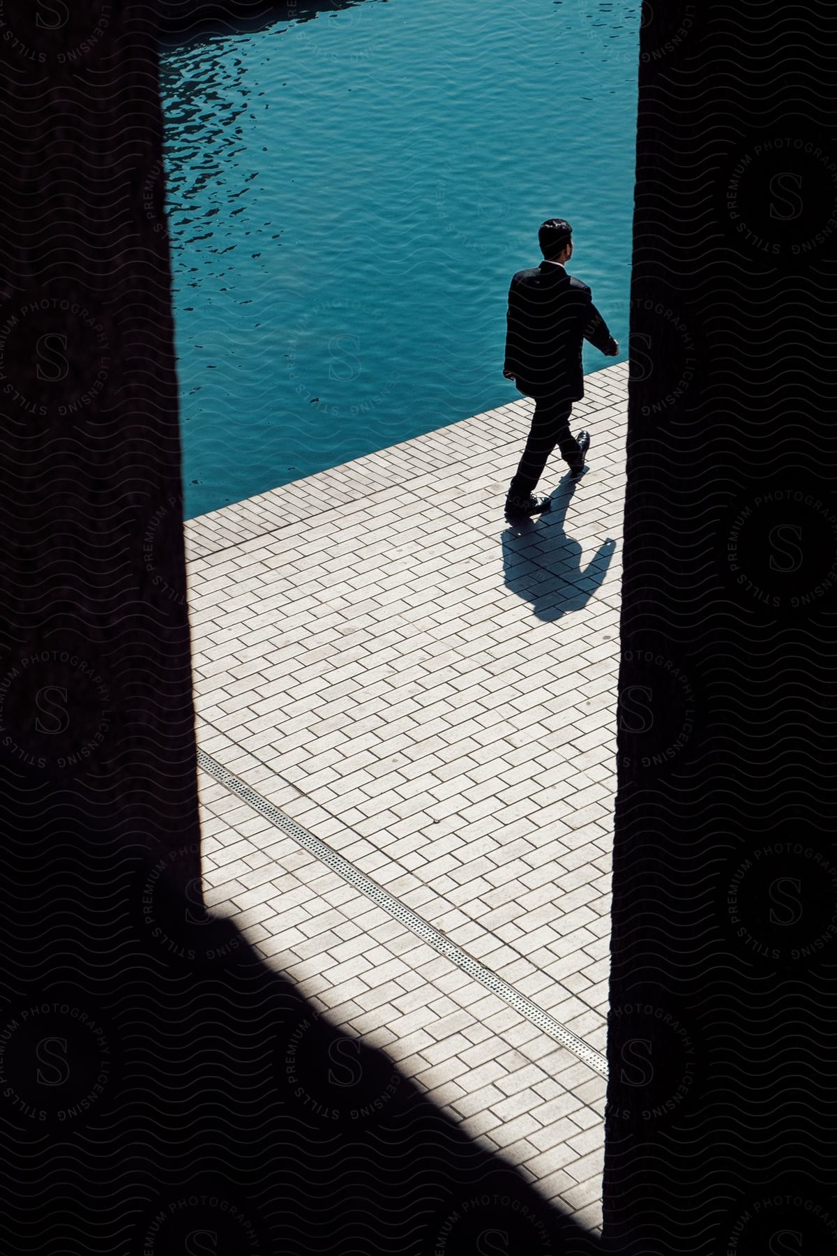 A man in a suit is walking along a promenade near the water