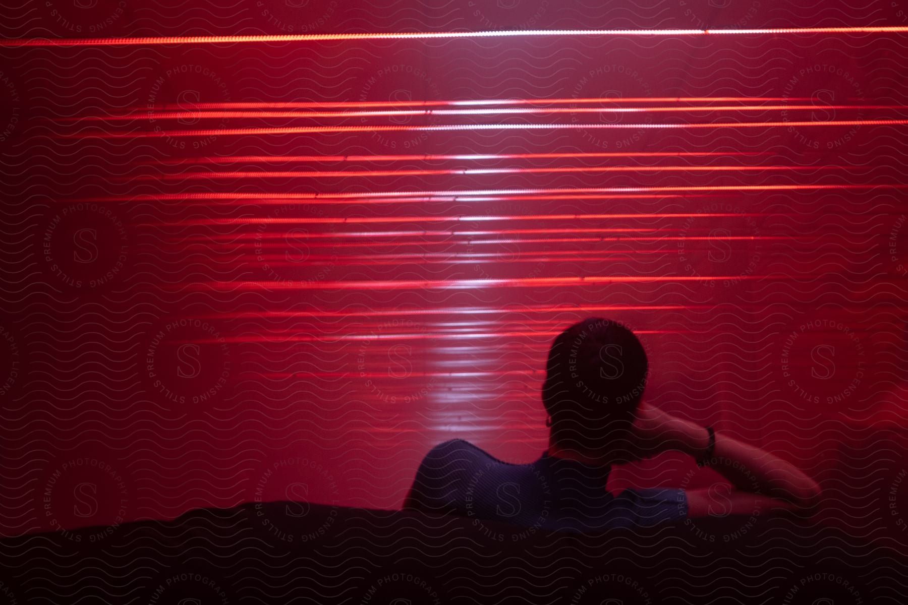 A man sitting on a couch in front of red lights resting his head on his hand