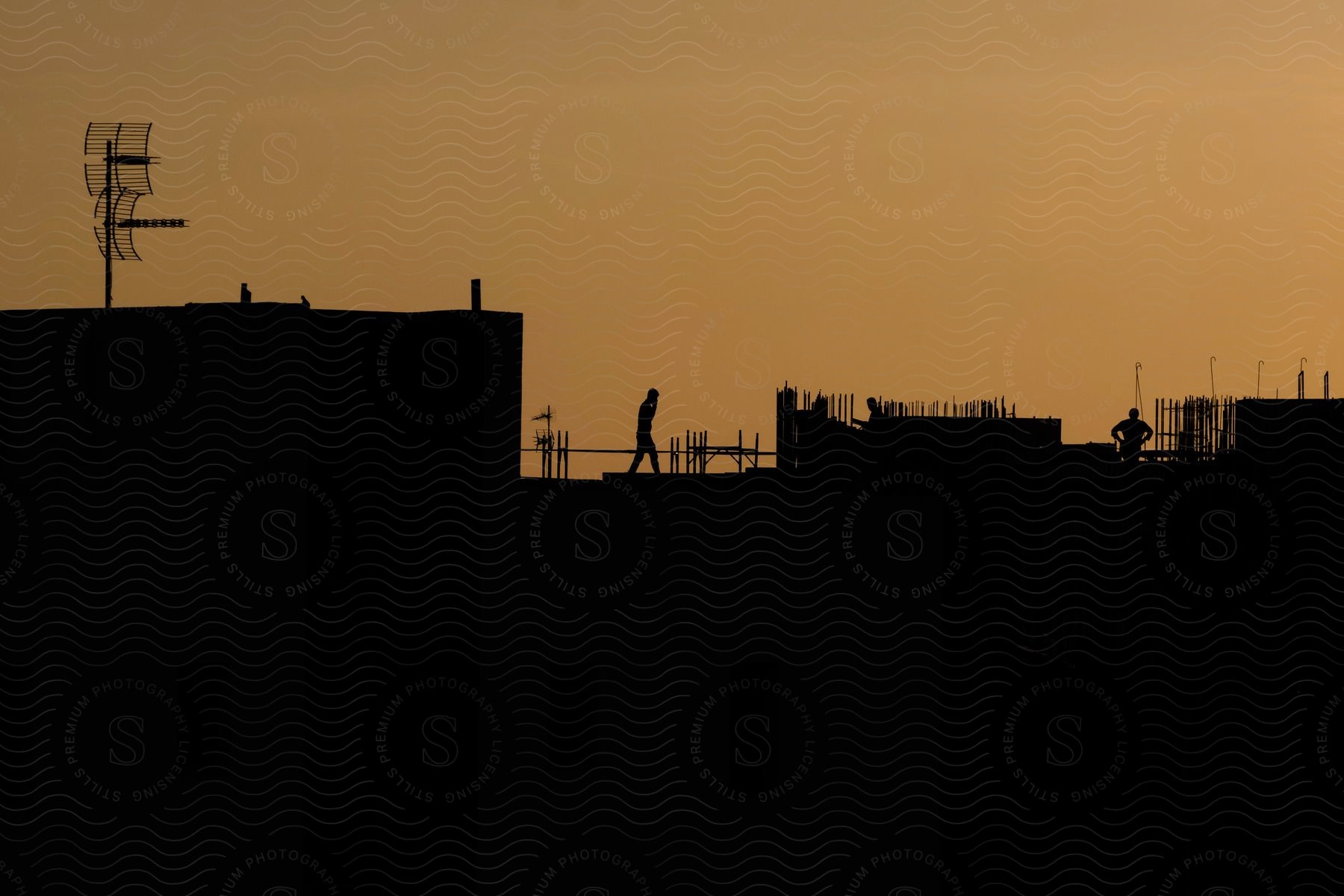 Two people on top of a structure with fence posts against an orange sky