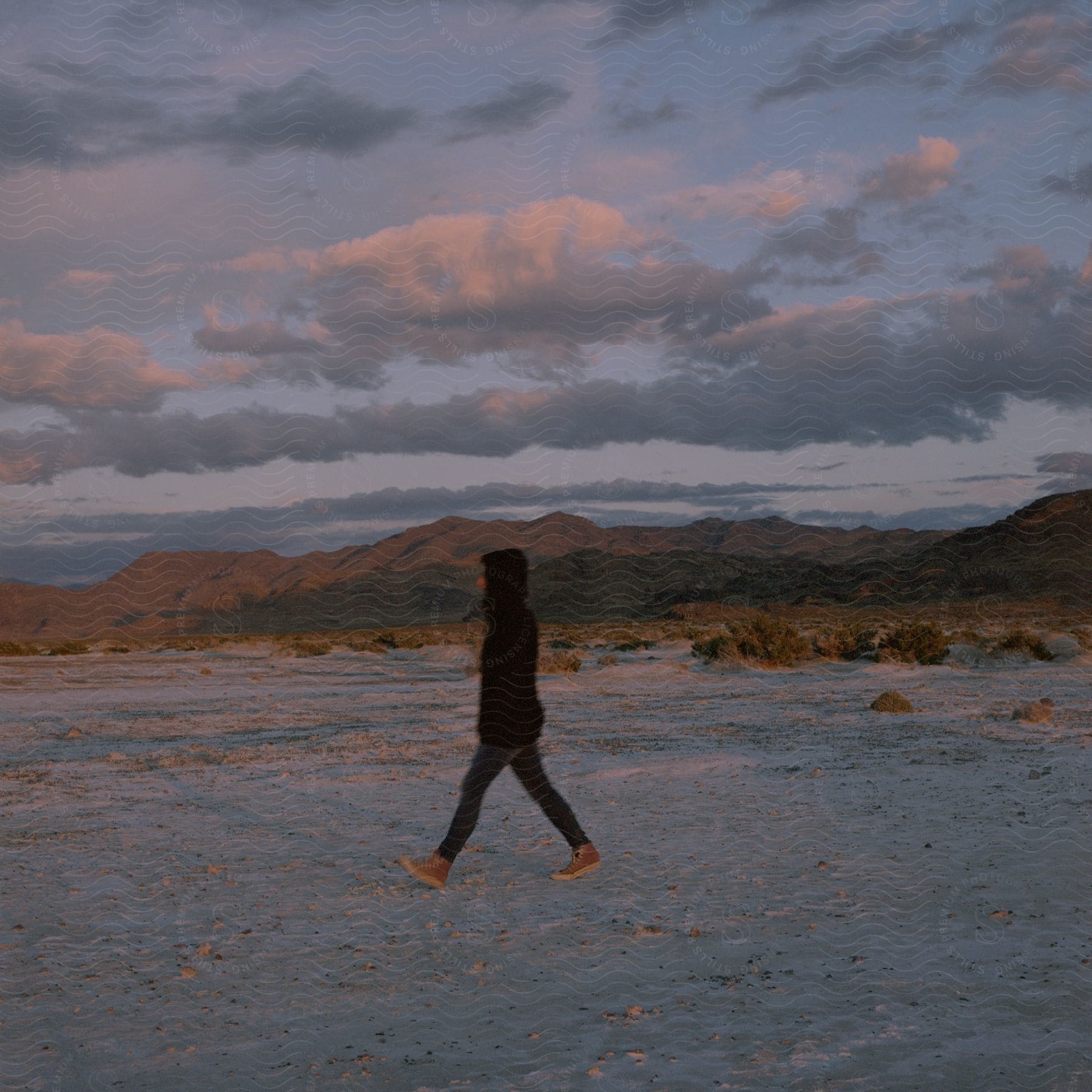 A young woman walks through a sandy desert with hills in the distance