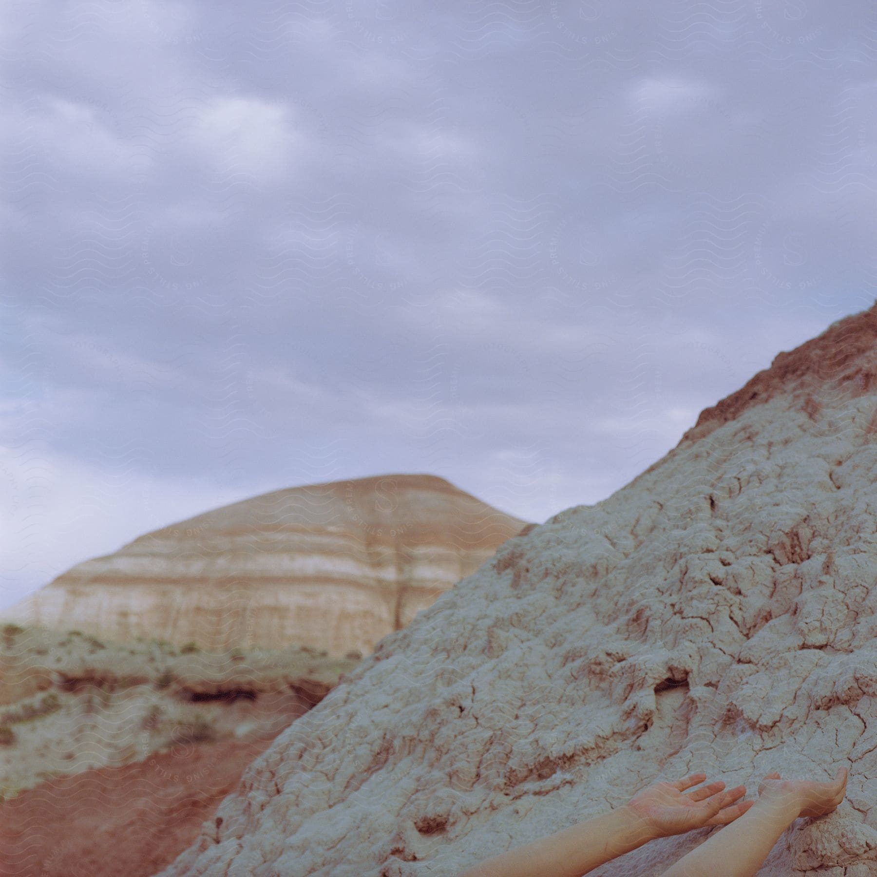 Stock photo of someones hands are reaching toward white rocks in desert badlands with rock cliffs