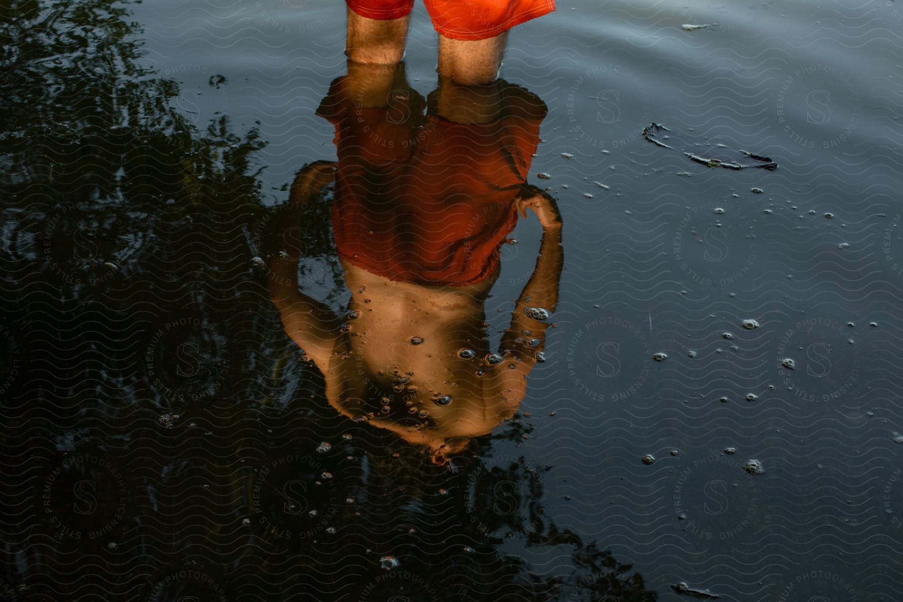 A male stands in kneedeep water with his reflection