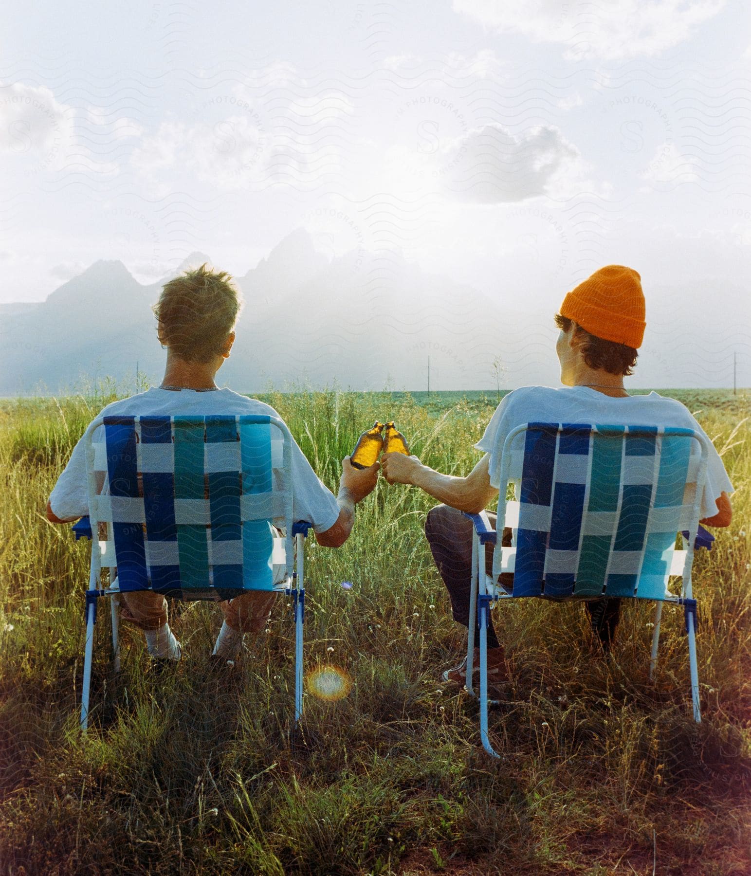 Stock photo of two friends sitting in a field enjoying each others company and tossing their drinks