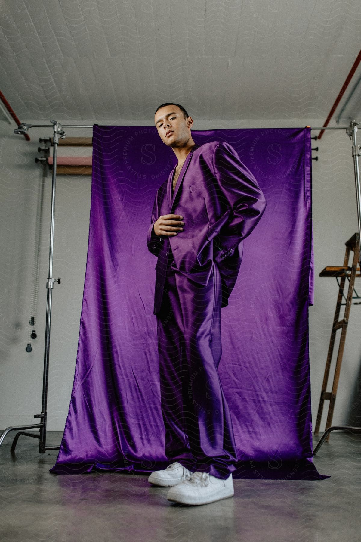 A man in a purple suit stands in front of a purple backdrop in a studio