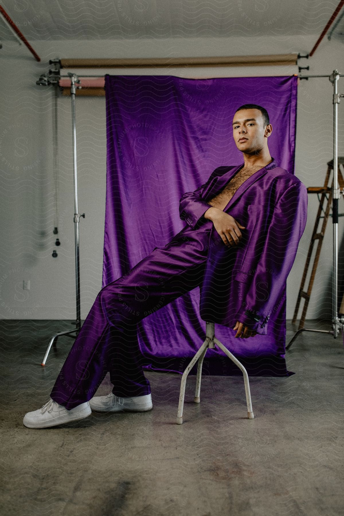A male model wearing a purple silk suit poses against a stool in an urban environment
