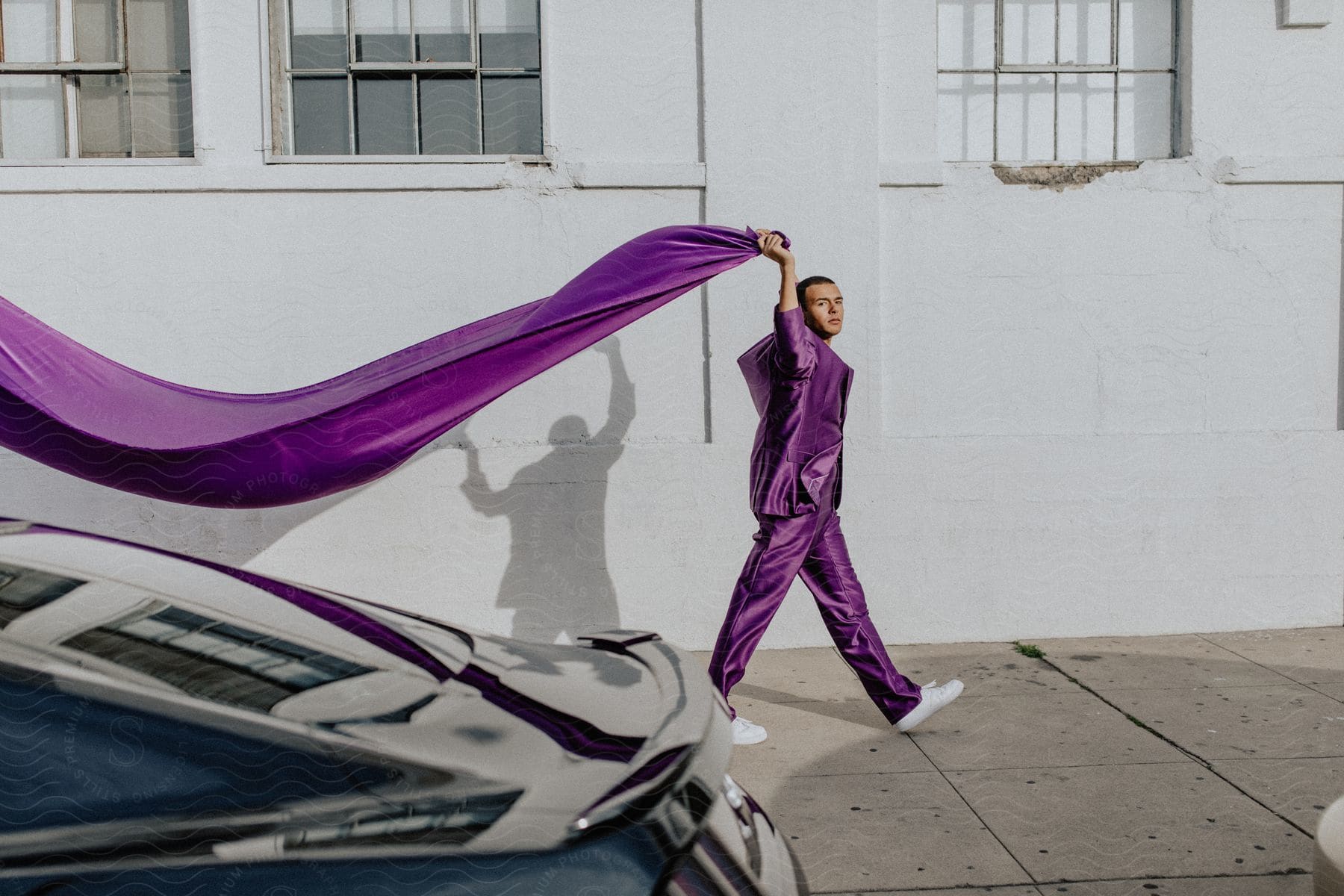 A person in neutral clothing stands in front of a purple car in the city