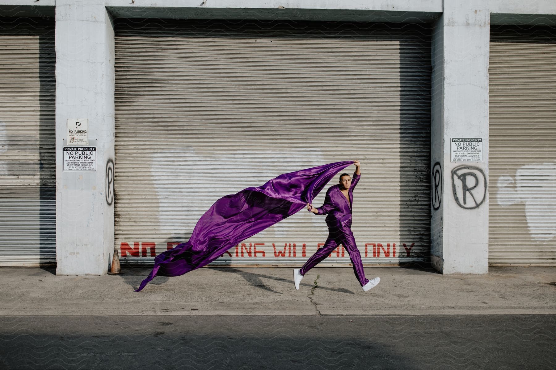 A man in a purple jumpsuit dances with a purple streamer behind him