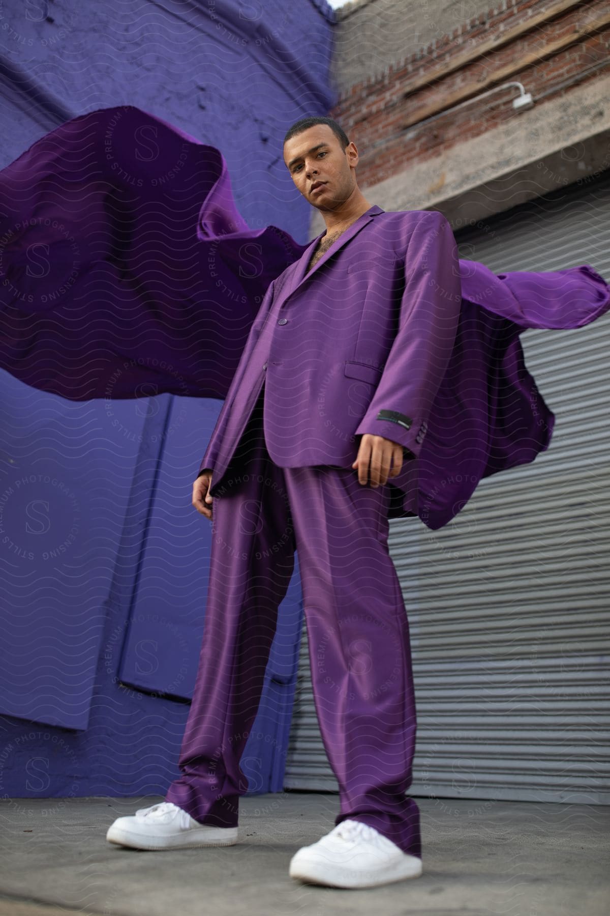 A man in a purple suit poses in a warehouse with a purple wall