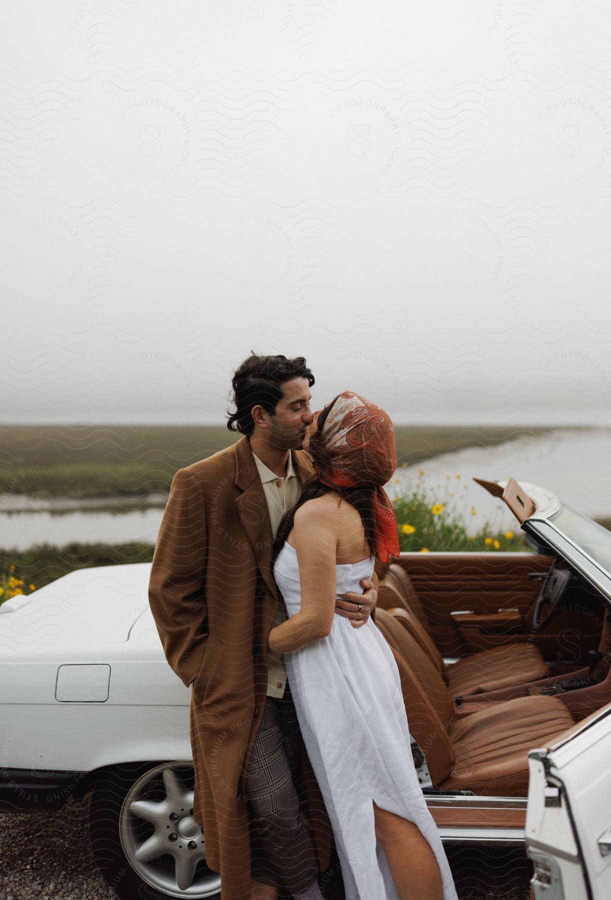 A couple kissing next to a car