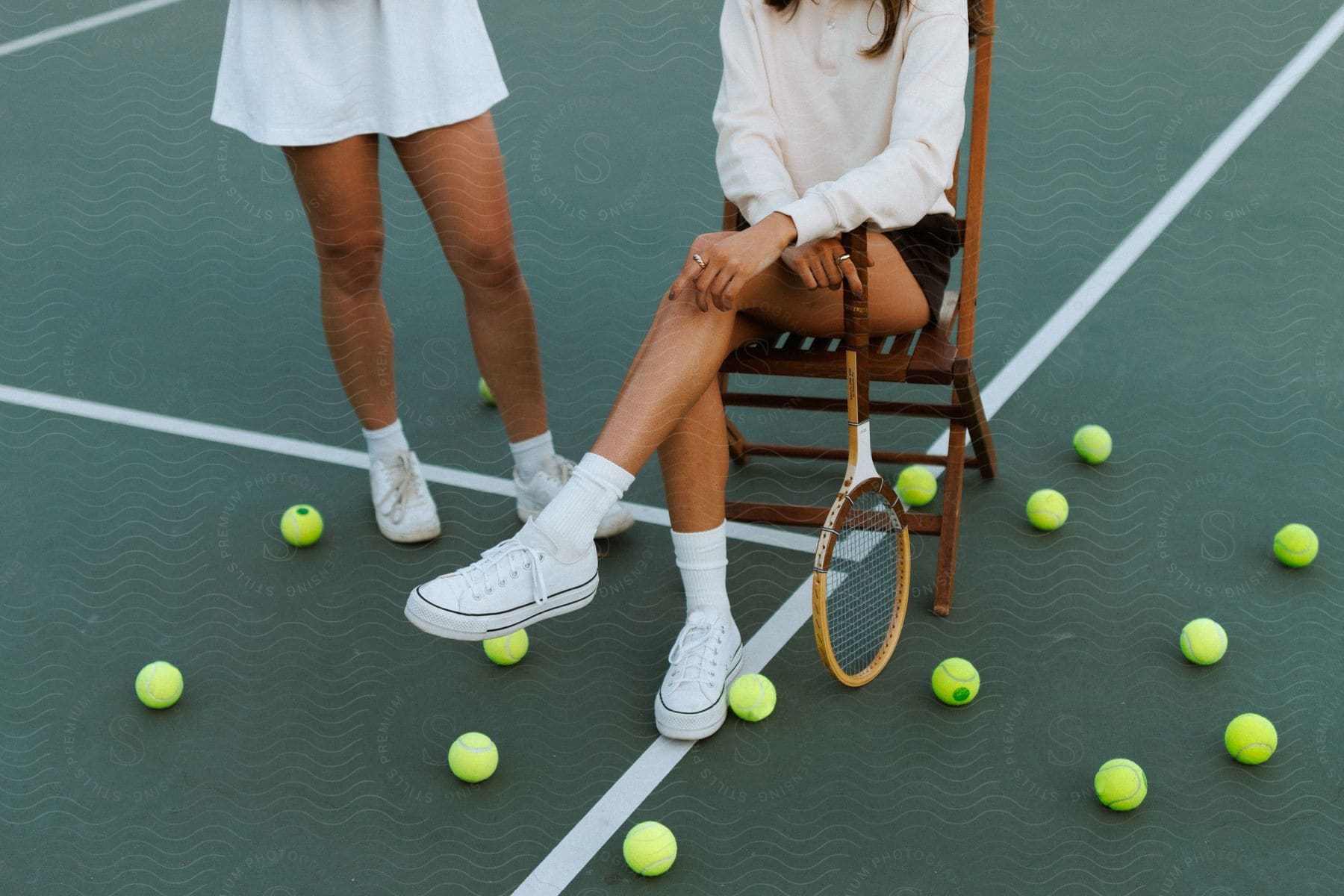 Two women on a tennis court one sitting in a chair and the other standing during the day