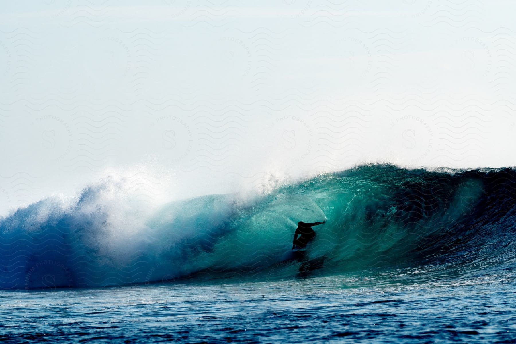 A surfer rides a wave on his surfboard in the blue sea with the sun glinting off the water